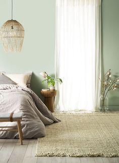 a bed sitting in a bedroom next to a window with white drapes on the windowsill