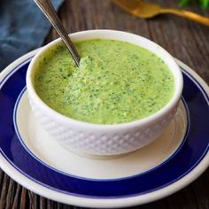 a white bowl filled with broccoli soup on top of a blue and white plate