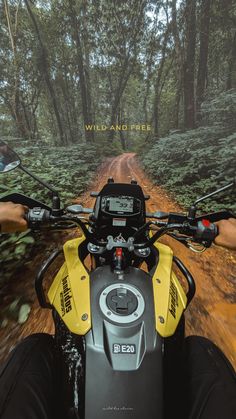 a person riding on the back of a yellow motorcycle down a dirt road with trees in the background