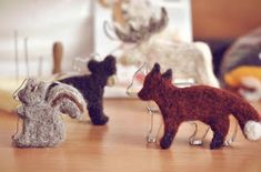 three small animal figurines sitting on top of a wooden table next to sewing needles