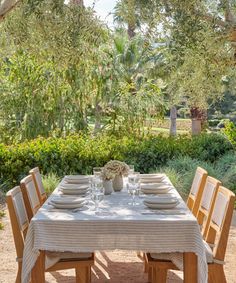 a table set with plates and glasses on it in the middle of a garden area