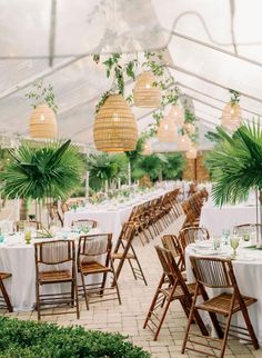 tables and chairs are set up in a tent for an outdoor wedding reception with greenery hanging from the ceiling