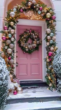 a pink door decorated with christmas ornaments and wreaths in front of the entrance to a house