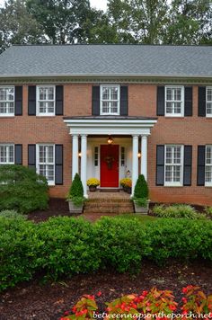 a large brick house with black shutters and red door in the front yard area