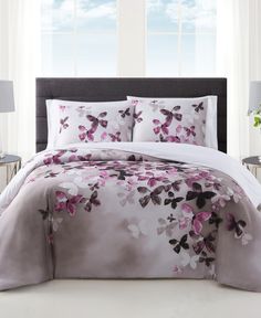 a bed with pink flowers on it in front of a white wall and two windows