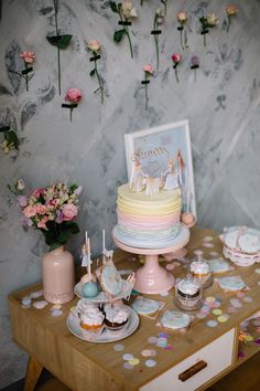 a table topped with cake and cupcakes next to a wall covered in flowers