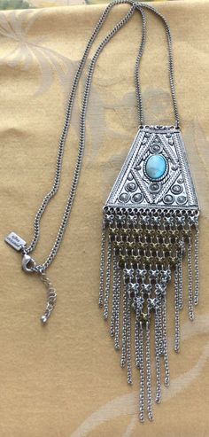 "Featuring this funky boho silver tone and brass pendant necklace with a faux turquoise accent. The pendant measures 8\" x 2-1/2\" and hangs on an adjustable silver tone chain. It measures from 29\" to 31\" and is in very good vintage condition. It looks like the turquoise stone was dyed and has faded over time. The original stone may be Howlite. The necklace is hallmarked \"American Eagle\"." Silver Bohemian Dangle Tassel Necklace, Bohemian Metal Tassel Necklace As Gift, Adjustable Silver Bohemian Tassel Necklace, Bohemian Silver Adjustable Tassel Necklace, Bohemian Adjustable Silver Tassel Necklace, Silver Bohemian Tassel Necklace, Bohemian Long Silver Turquoise Necklace, Bohemian Metal Tassel Necklace, Bohemian Turquoise Metal Pendant Necklace