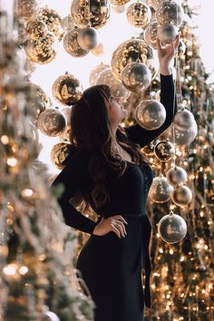 a woman standing in front of a christmas tree with lots of shiny balls hanging from it