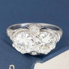 an antique three stone diamond ring on top of a blue book with a gold and silver clasp