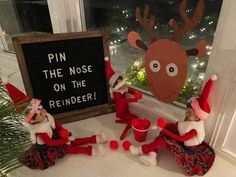 three elfs sitting in front of a sign that says pin the nose on the reindeer