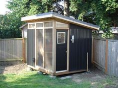 a small black shed sitting in the middle of a yard next to a wooden fence