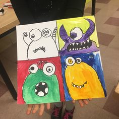 a child's hand holding up two different colored paintings with monster faces on them