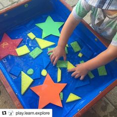 a young child playing with colorful tiles in a blue tray on the ground and hands reaching for them