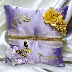 a purple pillow with a yellow flower and butterfly on the front, sitting on a white satin bed sheet