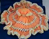 a crocheted doll sitting on top of a blue blanket with an orange dress