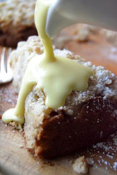 someone is pouring icing onto a piece of cake on a cutting board with a fork