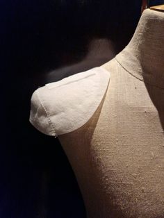 a mannequin with white fabric on it's back and neck, in front of a black background