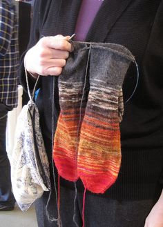 a person holding two pairs of knitted mitts in their hands and the other one with yarn on it