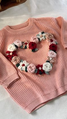 a pink sweater with flowers is laying on the bed