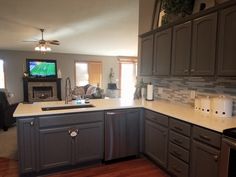 a kitchen with gray cabinets and white counter tops, an oven, dishwasher, microwave and television in the corner