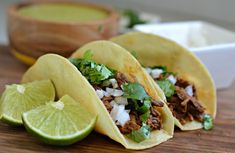 three tacos with meat, onions and cilantro on a wooden table next to a bowl