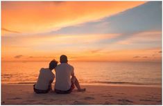 two people are sitting on the beach watching the sun set over the water and clouds