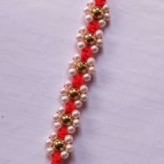 a red and white beaded bracelet with gold balls on it's end is shown