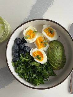 a white bowl filled with eggs, blueberries and greens next to a green smoothie