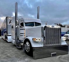 two large semi trucks parked next to each other in a parking lot on a cloudy day