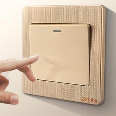 a person pressing the button on a wall mounted light switch with their hand pointing at it