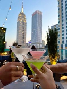 two people toasting with cocktails in front of the city's skyscrapers