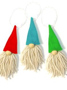 three christmas gnome hats with tassels are hanging from strings on a white background