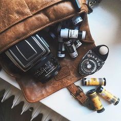 a brown leather bag filled with cameras and other items sitting on top of a white table