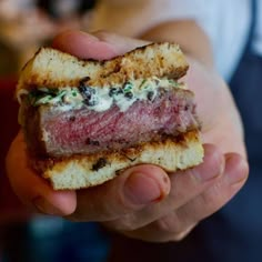 a hand holding a piece of bread with meat and cheese on it, in front of a blurry background