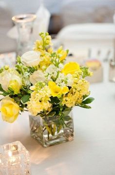 a vase filled with yellow and white flowers on top of a table next to candles