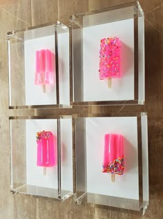 four popsicles in clear boxes with sprinkles and pink frosting on them