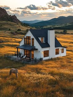 a horse grazes in front of a white house on a hill with mountains in the background