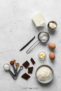 ingredients for chocolate cake laid out on a white counter top, including eggs, flour, butter, and other items