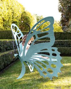 an image of a butterfly sculpture in the middle of a garden with hedges behind it