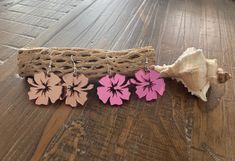 three pink flowers are sitting next to a piece of driftwood