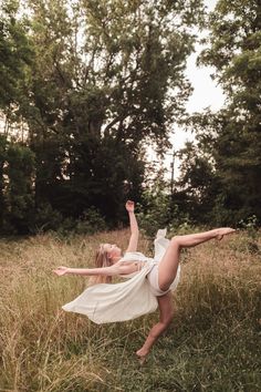 a woman in a white dress is doing a handstand on the grass by some trees