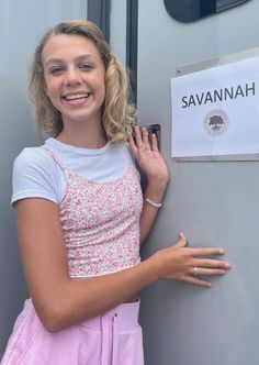 a woman standing next to a gray wall with a sign on it that says savannah