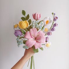 a hand holding a crocheted bouquet of flowers in pink, yellow and white