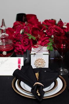 the table is set with black and gold plates, napkins, and red roses