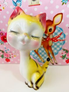 a yellow and white cat figurine sitting next to a pink wall