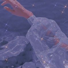 a hand reaching out from the water with sparkling stars in the sky above it and on top of some rocks