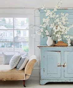 a blue cabinet with white flowers in it next to a couch and window sill