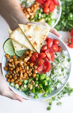 two hands holding a bowl filled with vegetables and pita bread