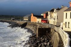 the waves are crashing against the rocks along the shore line as houses stand on either side