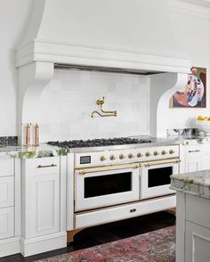 a kitchen with white cabinets and gold trimmings on the oven, counter tops